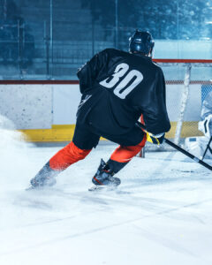 A hockey player wearing a black jersey with the number 30 and red pants skates on an ice rink, kicking up snow as they turn near the goal.